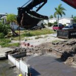 Excavator setting a new precast seawall panel from land on Fort Myers Beach