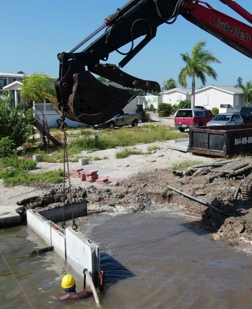 Excavator setting a new precast seawall panel from land on Fort Myers Beach